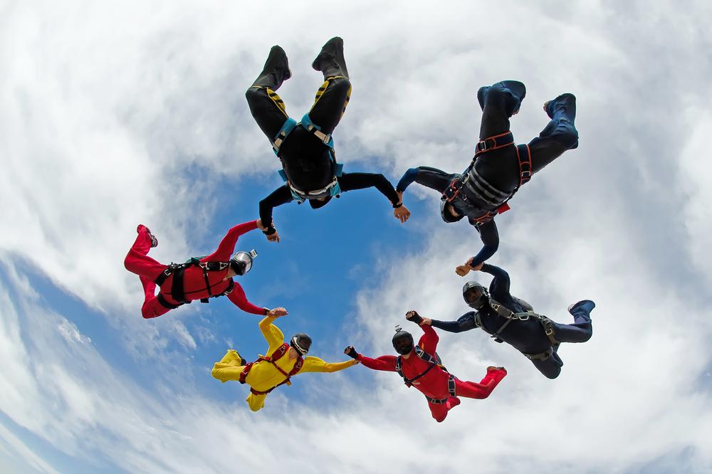 six skydivers linking hands against a cloudy sky